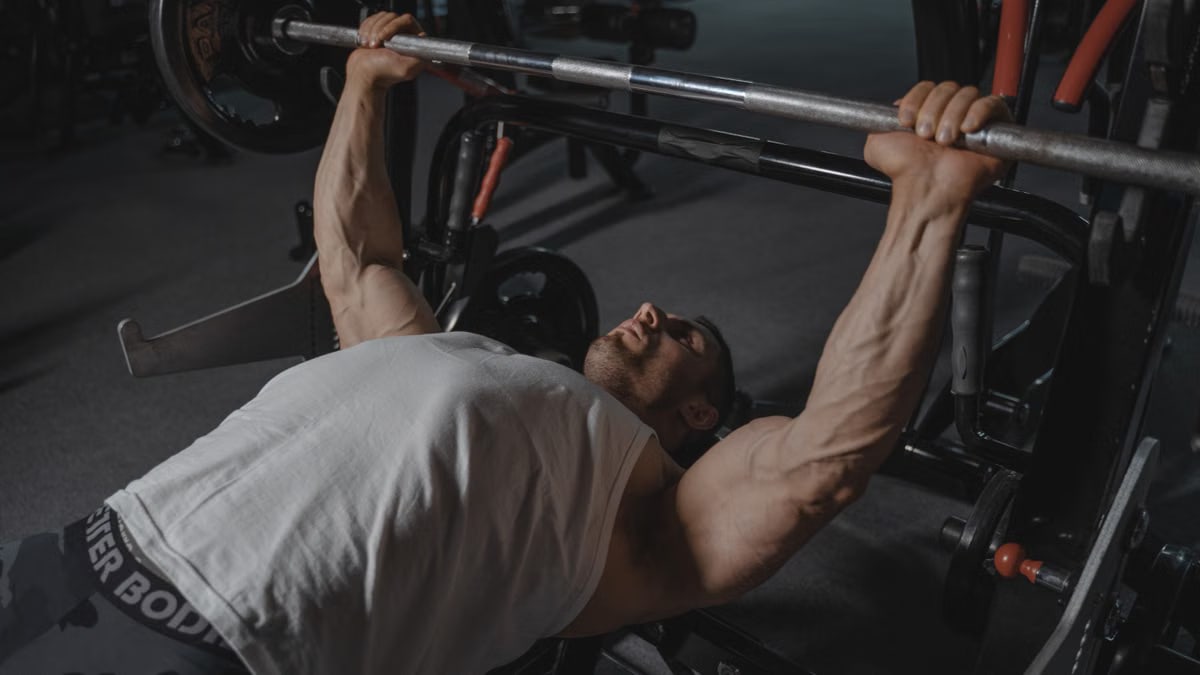 A focused man lifts heavy weights on a bench press machine in a dimly lit gym.